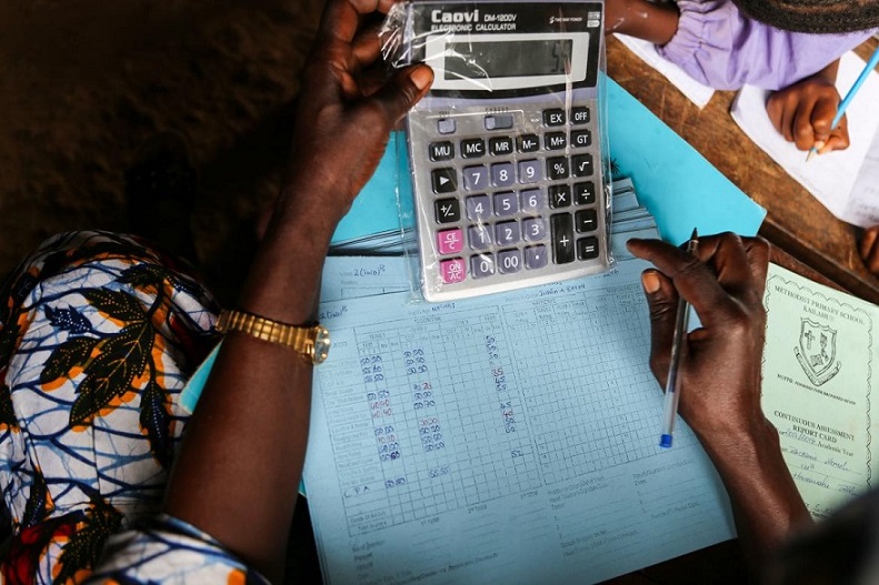 A teacher computes students' grades for their report card. Kailahun, Sierra Leone. 